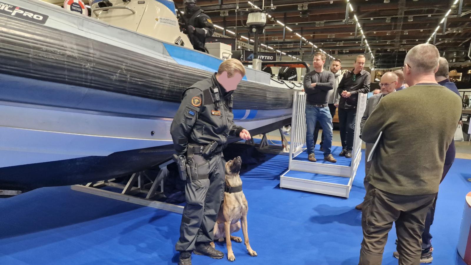 Rajavartija yhdessä rajajoiransa kanssa Rajavartiolaitoksen veneen edessä messuosastolla.