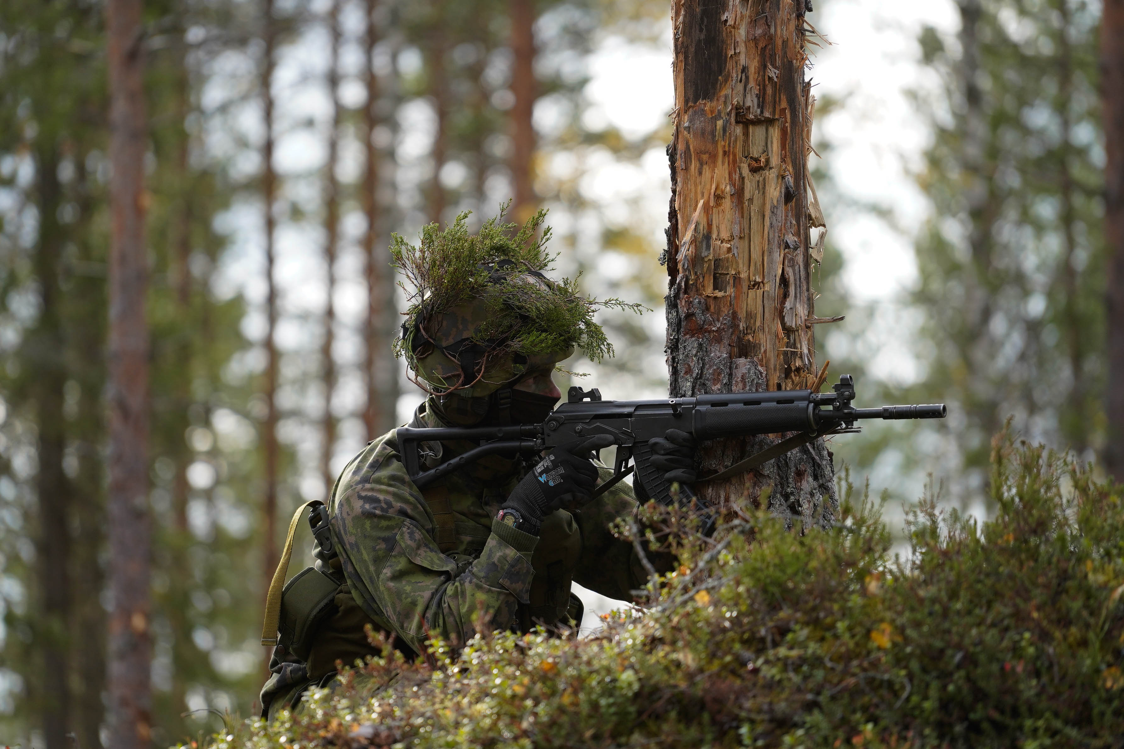 Sotilas tähtää aseella metsässä.