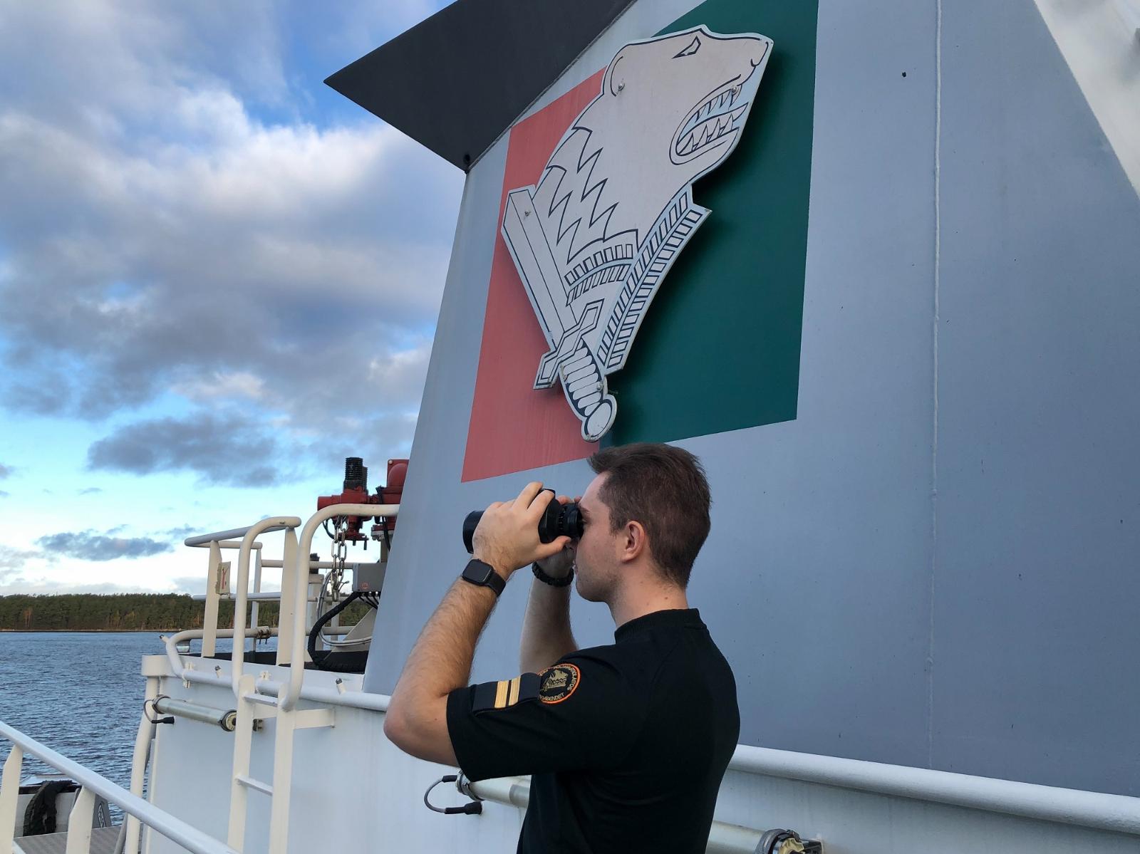En person tittar med en kikare på havet på ett bevakningsfartyg.