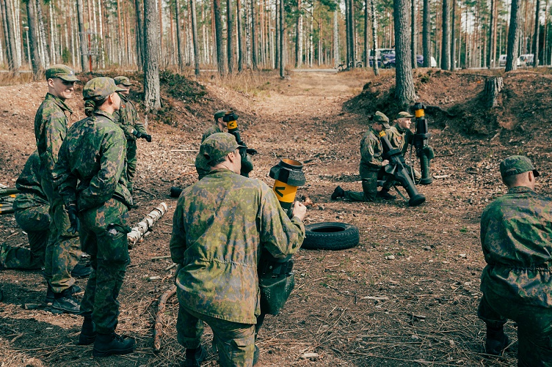 Ryhmä sotilasasuisia henkilöitä putkenmallisten aseiden kanssa mäntymetsikössä.