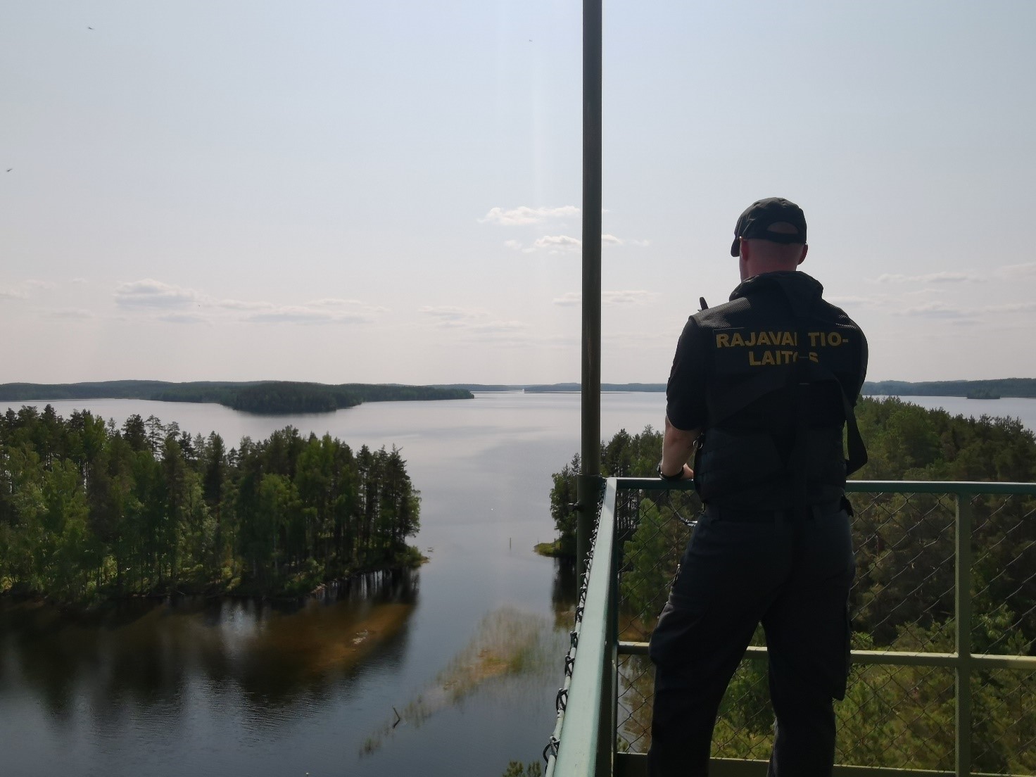 Rajavartija seisoo tähytystornissa. Taustalla näkyy järvimaisema.