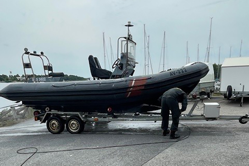 Bilden är tagen från sidan. Sjöbevakningsektionens hjälpbåt lyft upp från vattnet på en trailer. Framför båten står en person från sjöbevakningen böjd neråt med blicken mot marken.