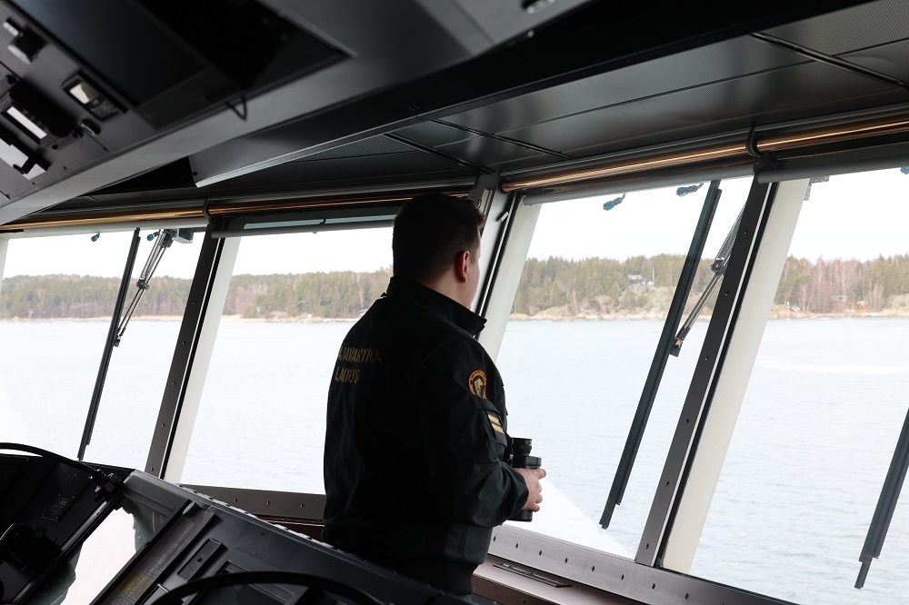 Sjövaktare är inne i en båt och tittar ut genom fönstret med en kikare i händerna.