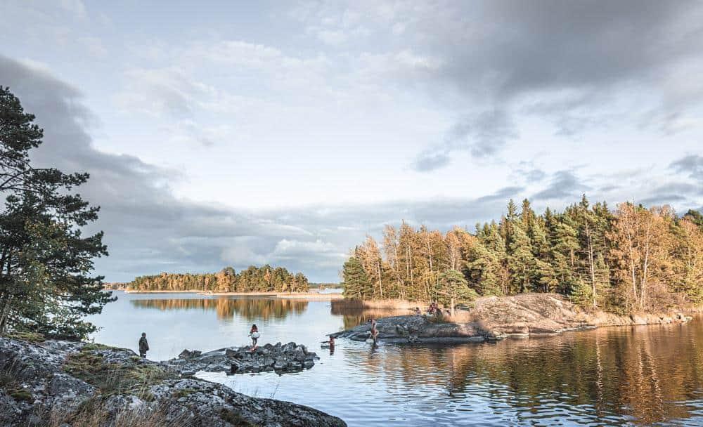 Kandidater simmar till ön när solen går upp. I bakgrunden träd, klippor och havet