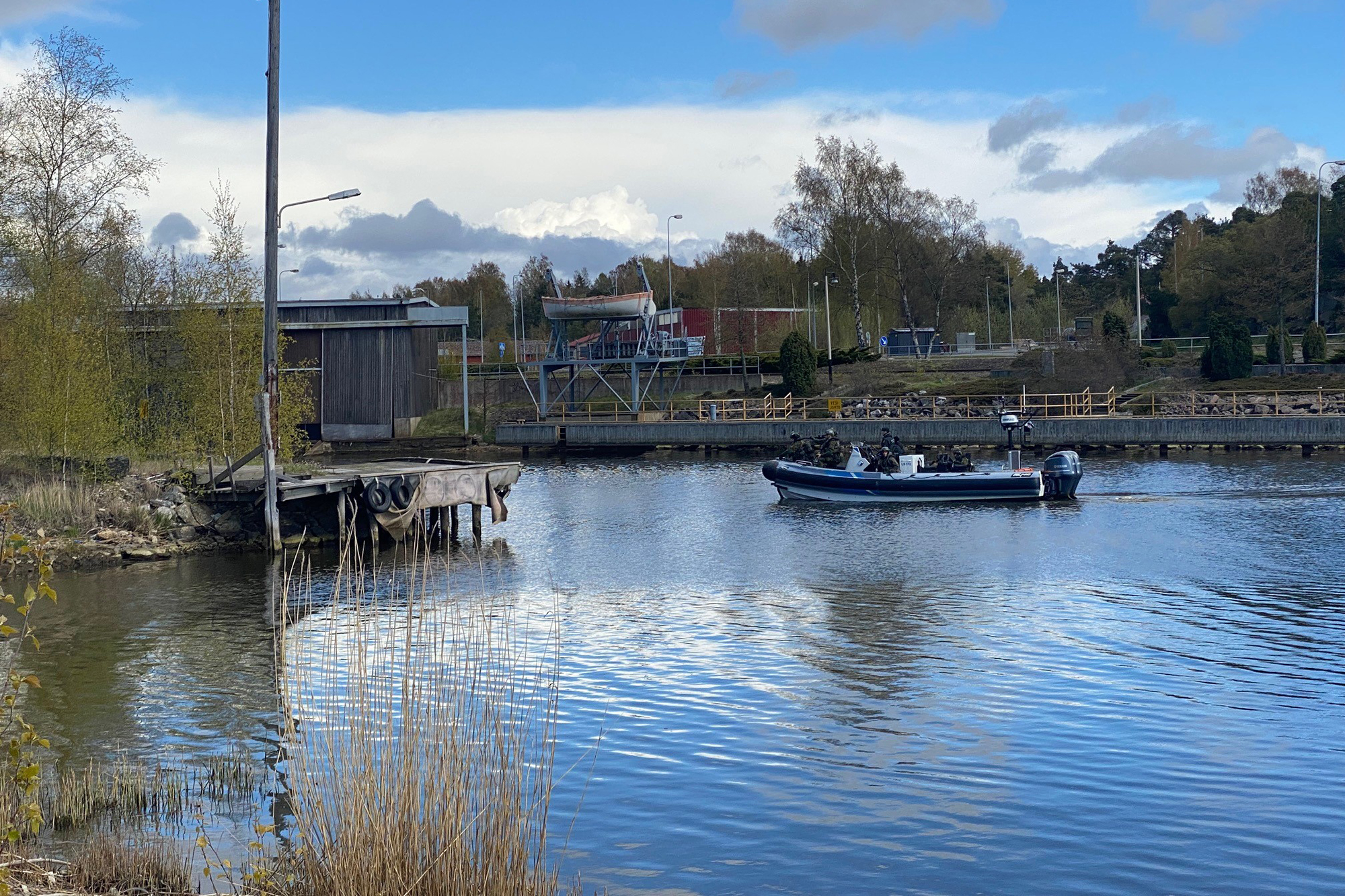 Bilden är tagen från sidan under en övningssituation. Fem stycken personer klädda i kamouflage sitter i en motorbåt. Alla har hjälp på huvudet och siktar framåt med sina vapen. 