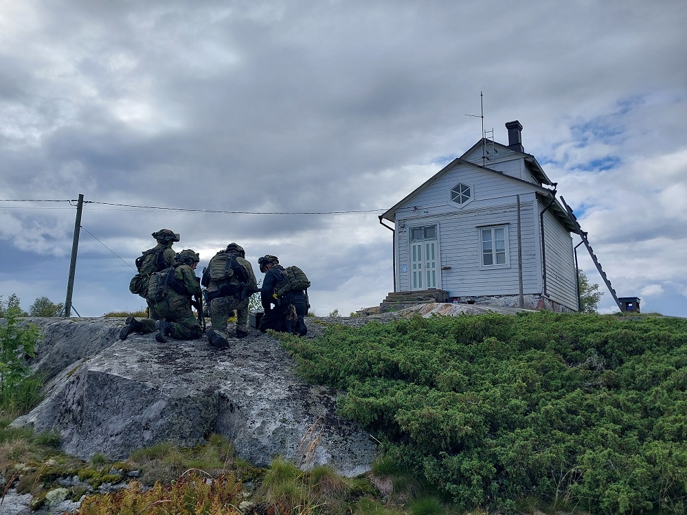 Ett hus på en ö. Nära huset finns det människor som övär militärt försvar. 