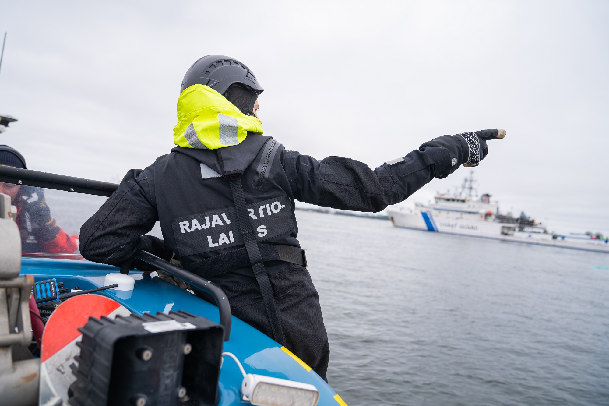 En person stannar på båten och pekar till höger. Det finns också en vit fartyg bakom honom. 