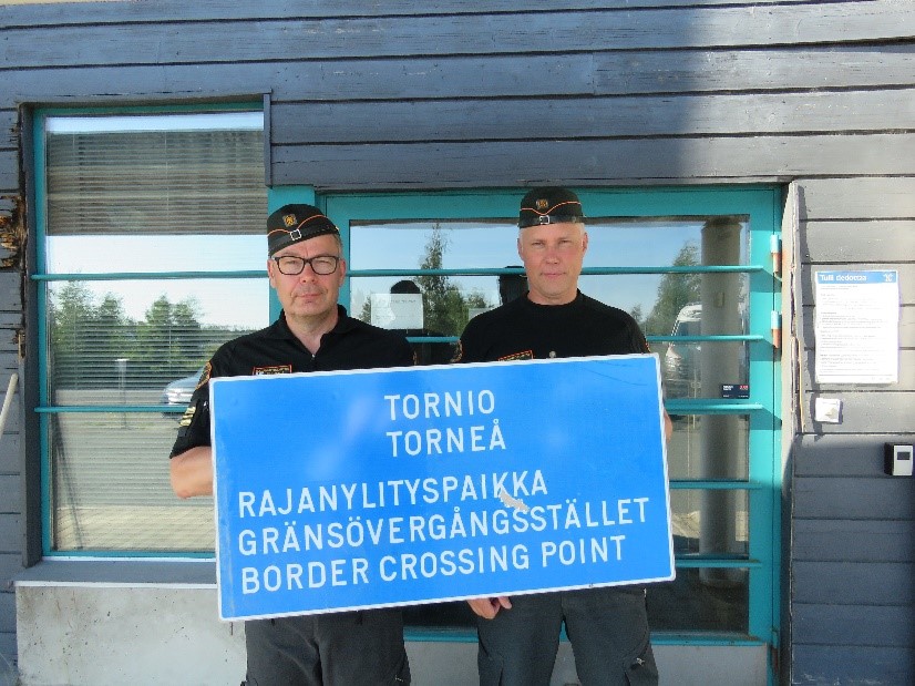 Kaksi rajavartijaa pitelevät kylttiä jossa lukee Tornio, rajanylityspaikka.
