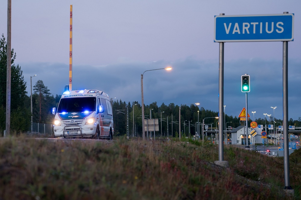 Partioauto illalla auringon laskettua. Taustalla näkyy rajanylityspaikka ja kuvan etualalla kyltti jossa lukee Vartius.