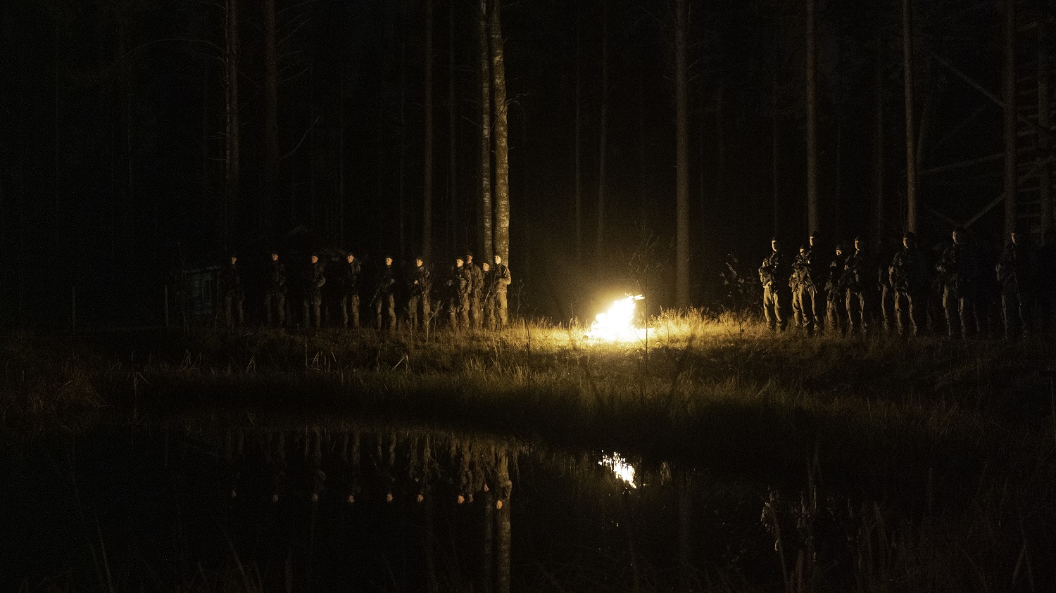 Erikoisrajajääkärikokelaat nuotion ympärillä yöllä. Etualalla näkyy lampi.