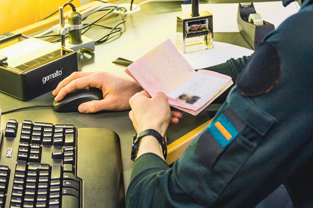 Rajavartija istuu tietokoneen edessä ja tarkastaa passia.
