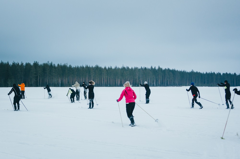 Ihmisiä hiihtää pellolla. Taustalla metsää.