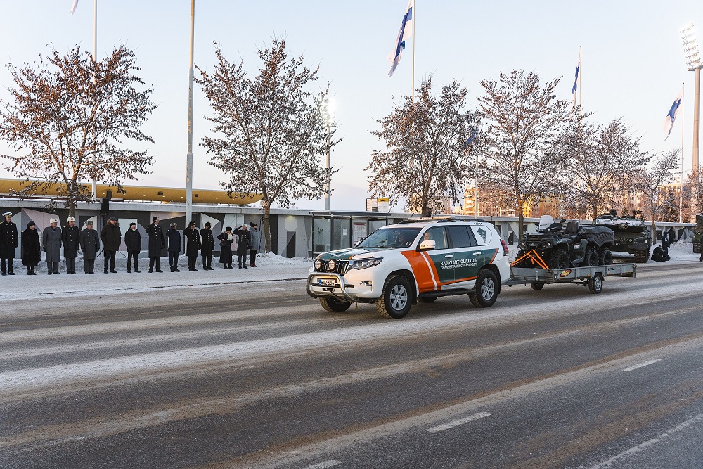 Rajavartiolaitoksen maastoauto vetää perässään peräkärryä paraatissa.