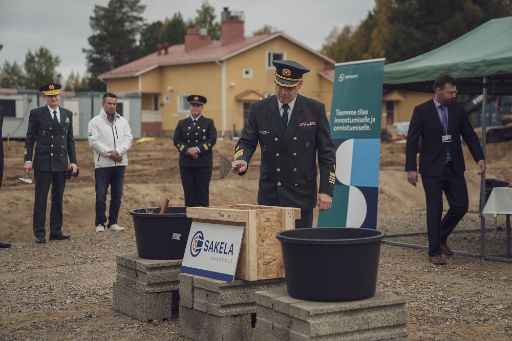 Muuraustilaisuus jossa yksi ottaa laastia lastalla ja muut katsovat taustalla.