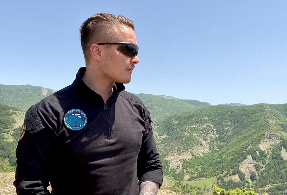 En sidoprofil av en officer som bär solglasögon. Det finns berg i bakgrunden.