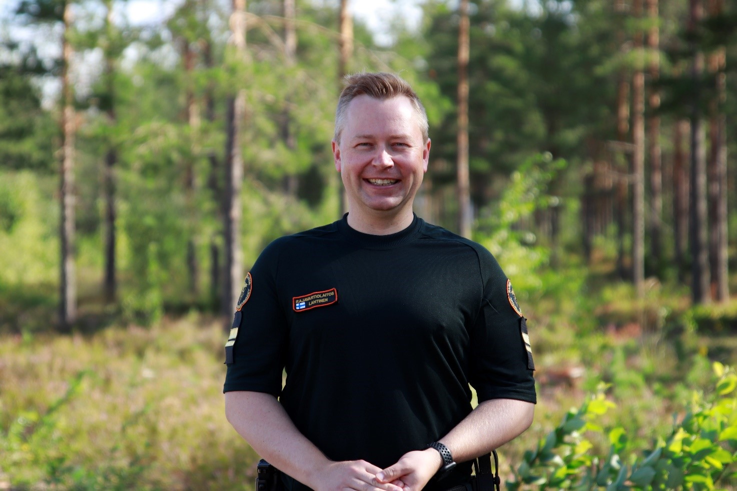 Jouni Lahtinen seisoo ja katsoo hymyillen kameraan. Taustalla on metsää.