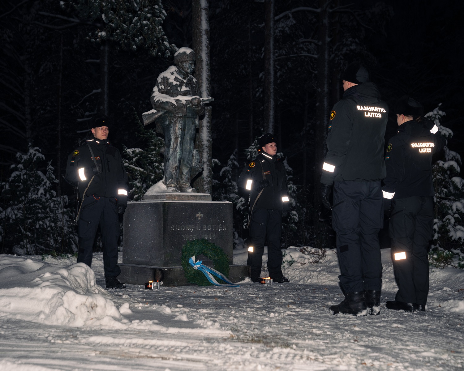 Två personer på vakt bredvid statyn. Två står framför statyn. Det ligger snö på marken och det är mörkt.