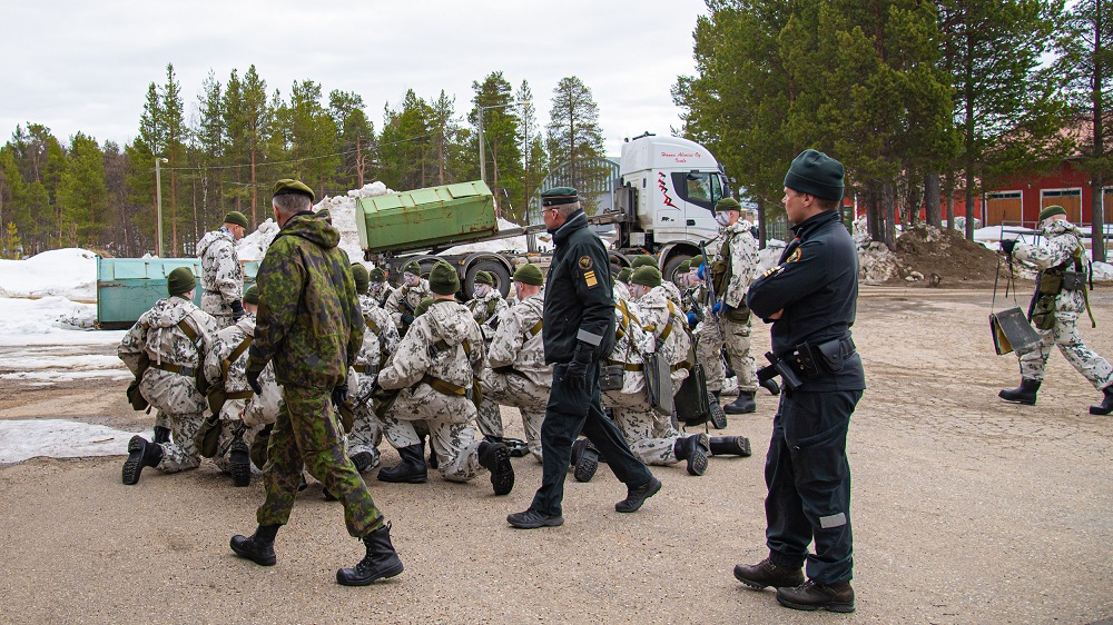 Rajavartiolaitoksen päällikkö ja Puolustuvoimien komentaja kävelevät. Kuvassa varusmiehiä harjoittelemassa. Taustalla rekka-auto.