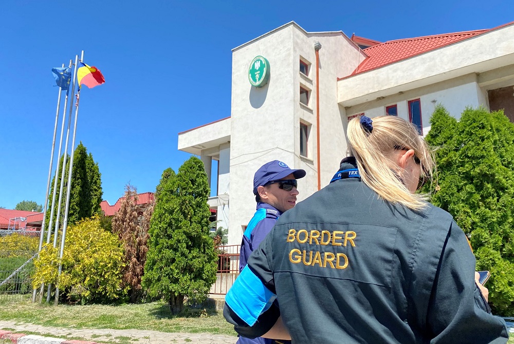 Kaksi rajavartijaa seisovat vaalean rakennuksen edessä. Taustalla näkyy pensaita ja EU:n ja Moldovan lippu.