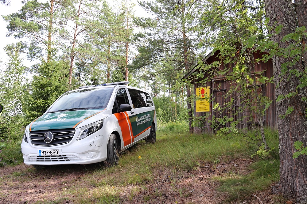 Partioauto metsämaisemassa. Takana näkyy keltainen rajavyöhykekyltti.