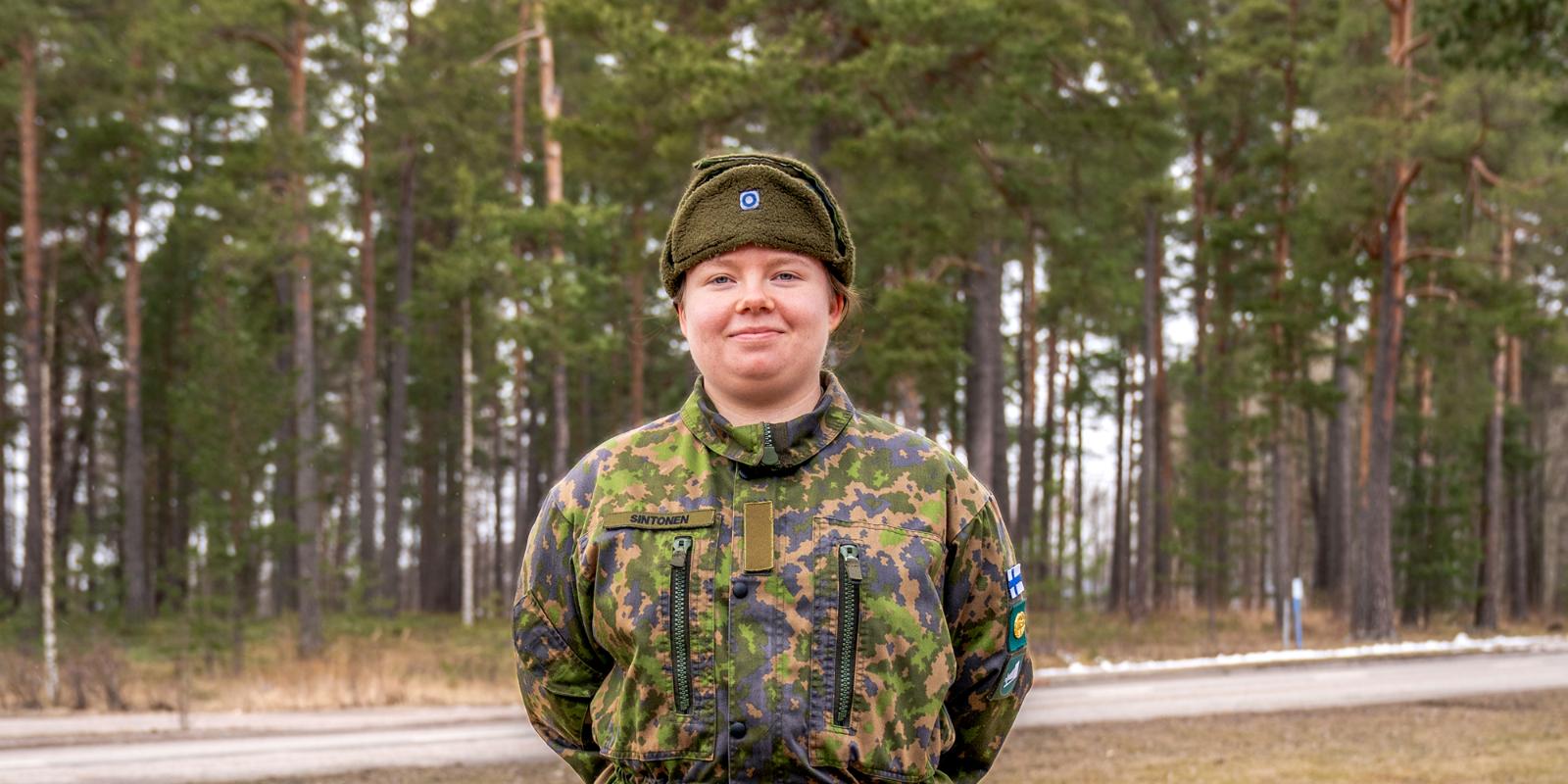 Viestintävarusmies Roosa Sintonen seisoo keväisen metsikön edessä ja katsoo kameraan.