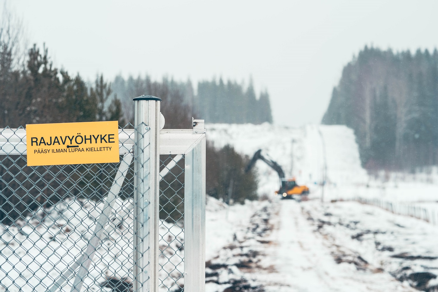 Talvinen maisema jossa kuvan etualalla portti ja kyltti jossa lukee rajavyöhyke. Taustalla näkyy kaivinkone.