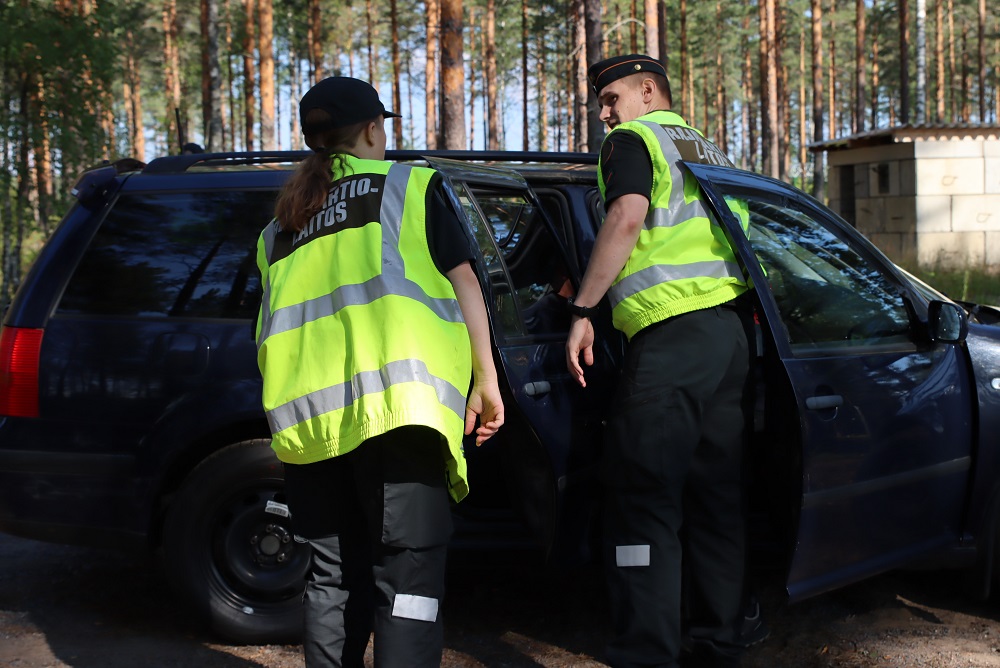 Kaksi henkilöä, joilla on keltaiset huomioliivit, tarkastavat henkilöautoa.
