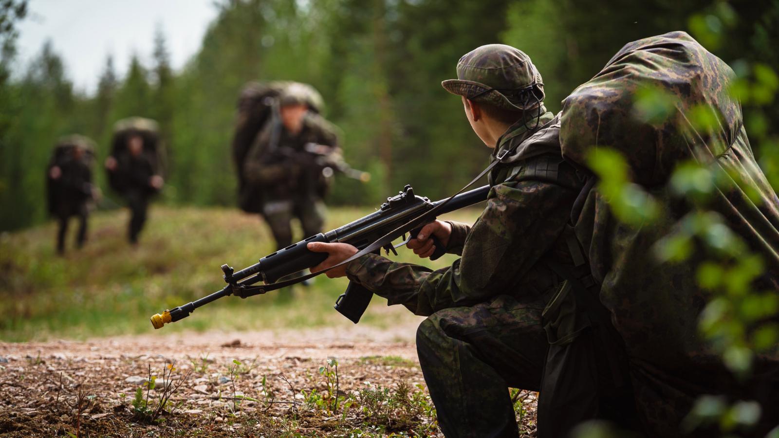 Rajajääkäri on maassa polven varassa ja vahtii ryhmäläisten ylittäessä tietä.