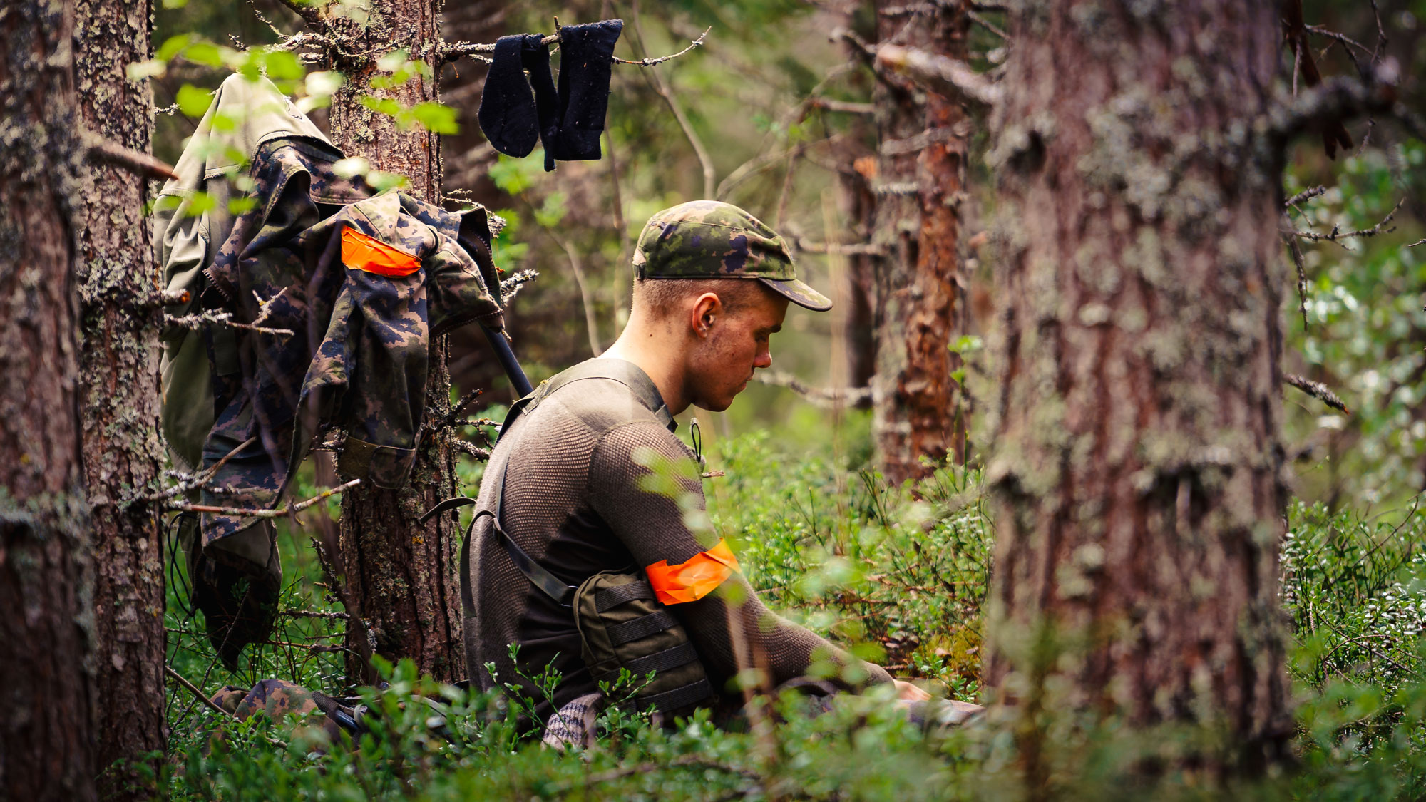 Rajajääkäri istuu metsän keskellä tauolla ja on ripustanut vaatteita kuivamaan puihin ympärilleen.