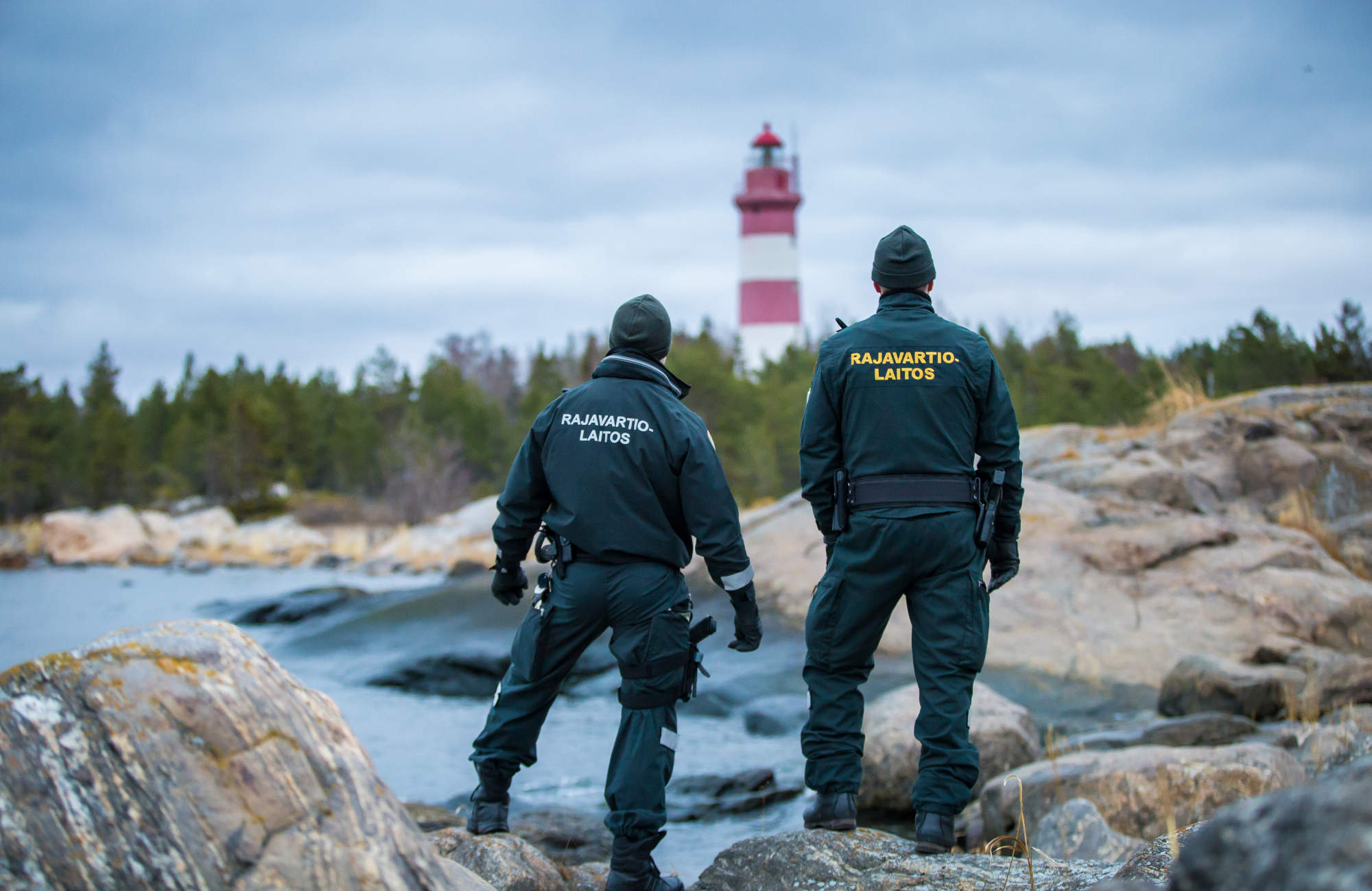 Två sjöbevakare står på klippan och tittar mot fyren.