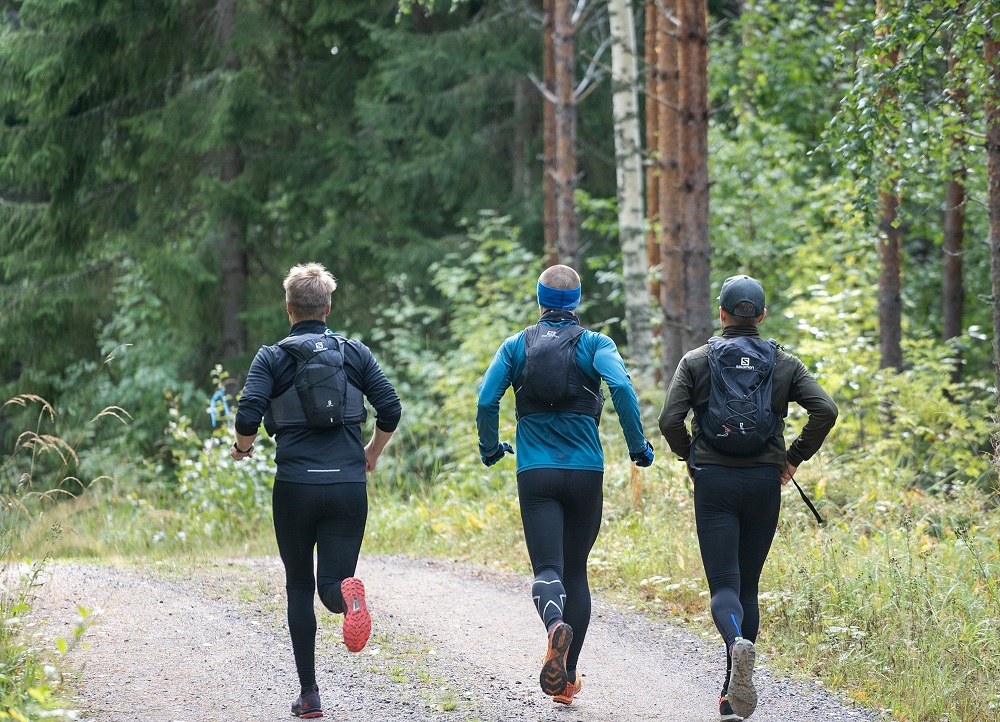 Kolme henkilöä juoksee metsätiellä urheiluvarusteissa. Kuva otettu takaapäin. 