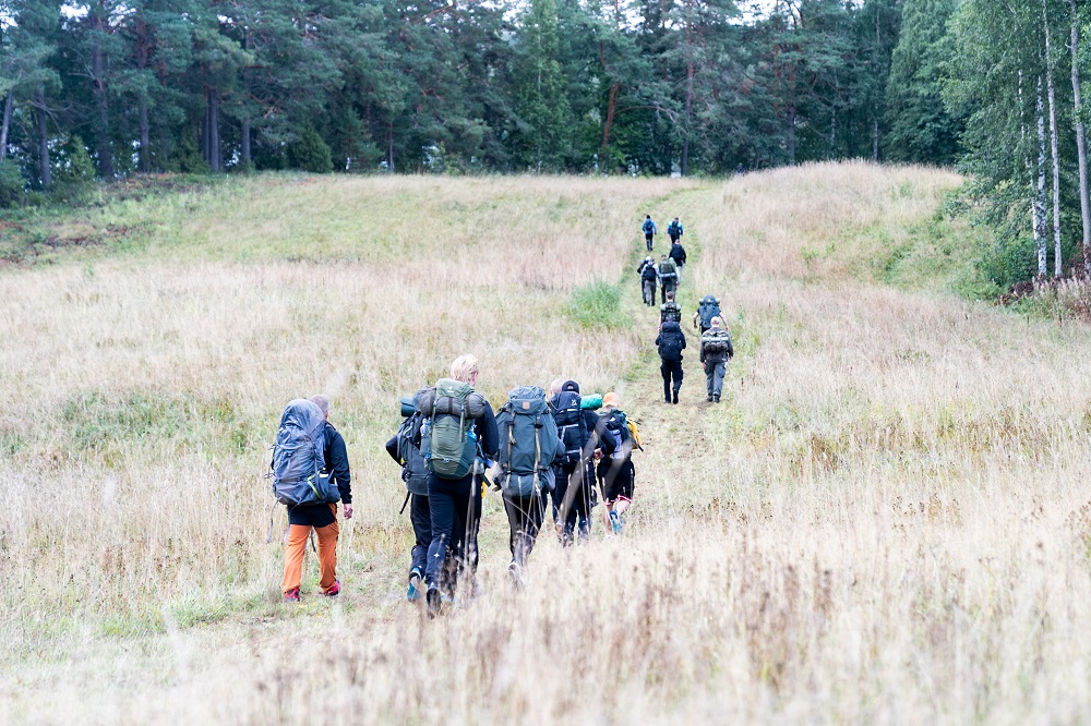 Ihmiset kulkevat reput selässä pellon läpi vievällä leveällä polulla.