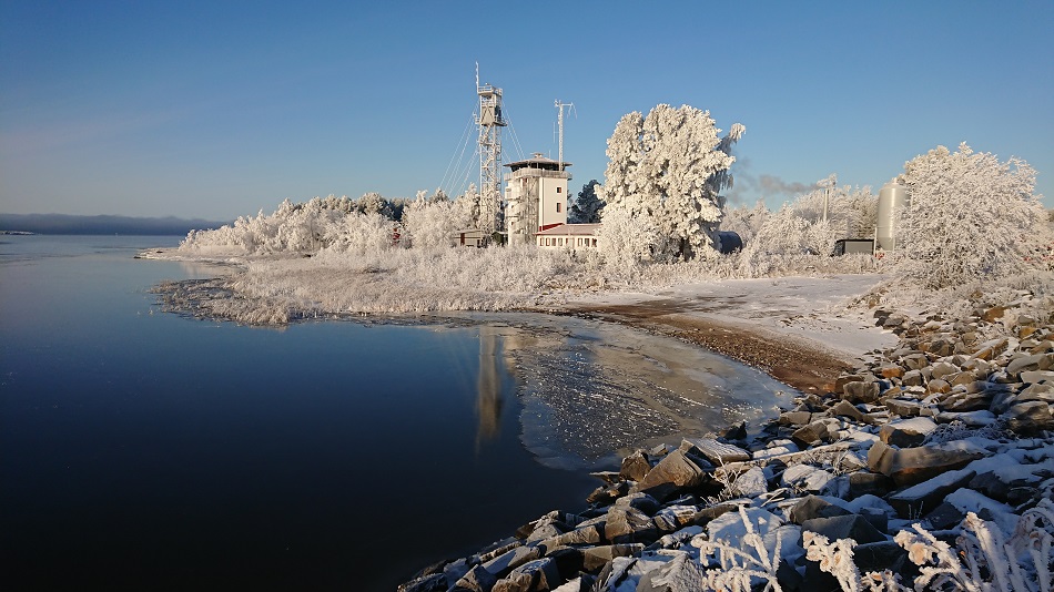 Virpiniemen merivartioaseman rakennukset talvisessa auringonpaisteessa. Maassa on lunta ja sula meri on rakennusten edessä.