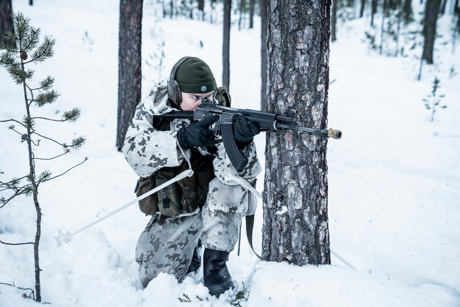 Rajajääkäri tähtäämässä polviasennosta puun takaa