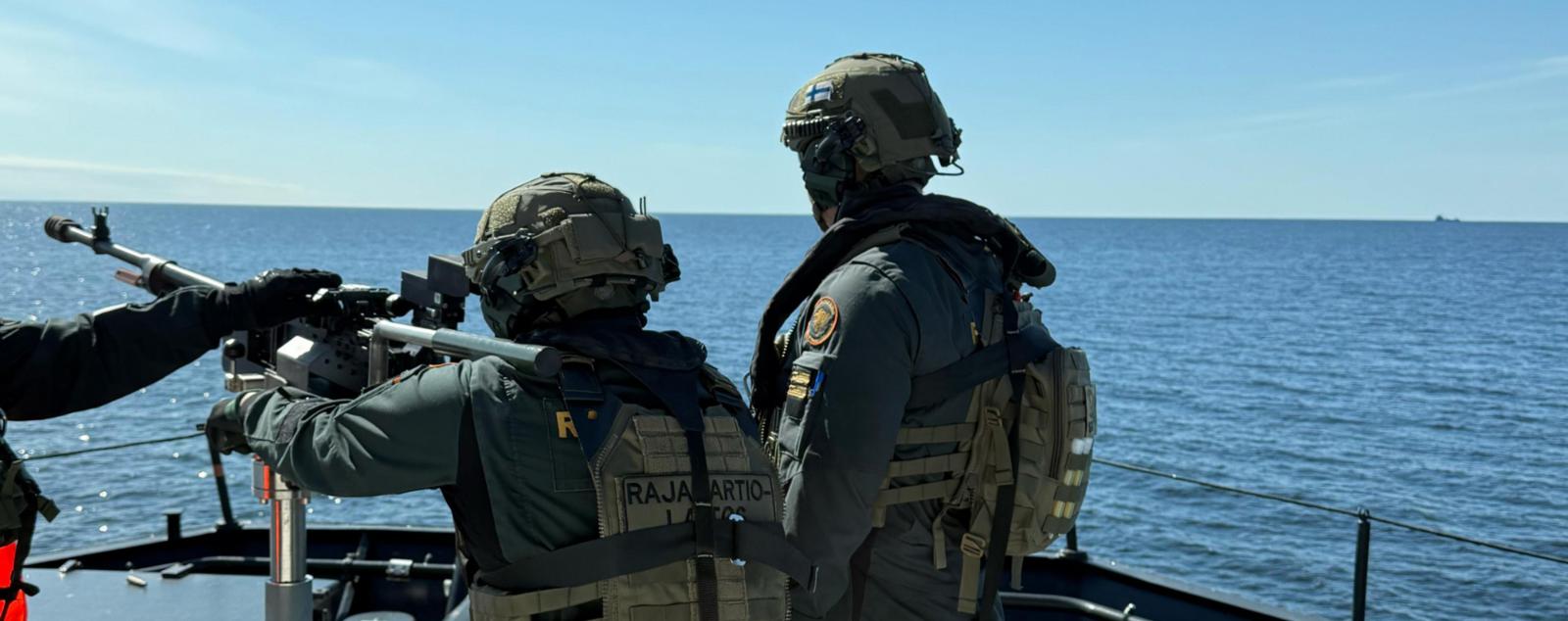 Två värnpliktiga står på däcket på ett patrullfartyg med ryggarna mot kameran och avfyrar en fartygsmaskingevär mot horisonten.